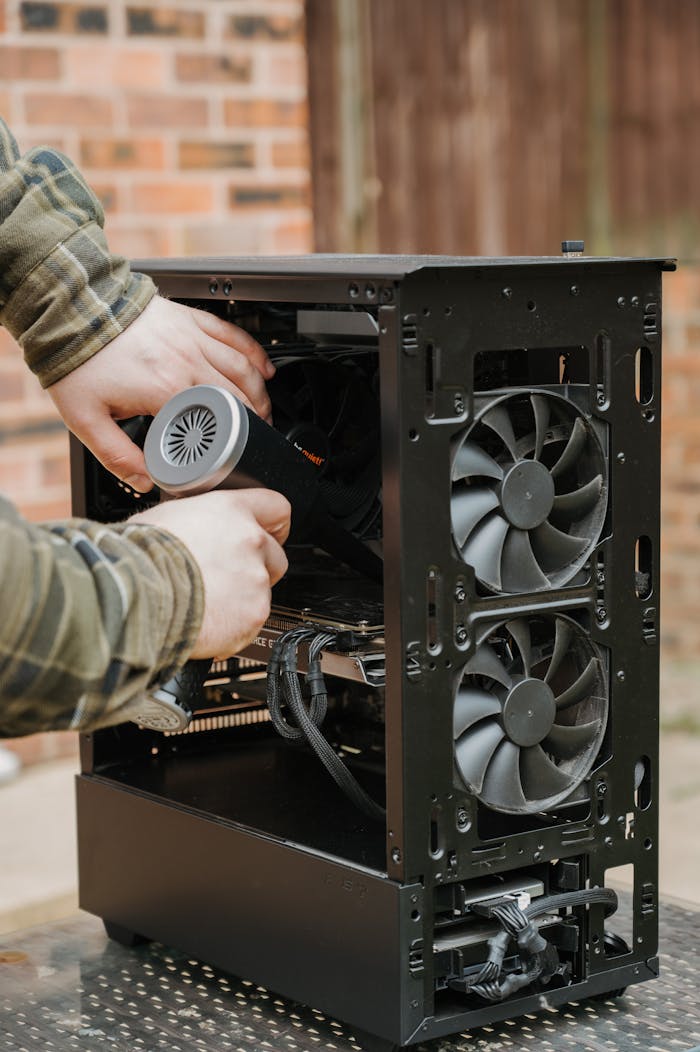 our-services-3 Hands cleaning a desktop PC case with an electric duster outdoors.