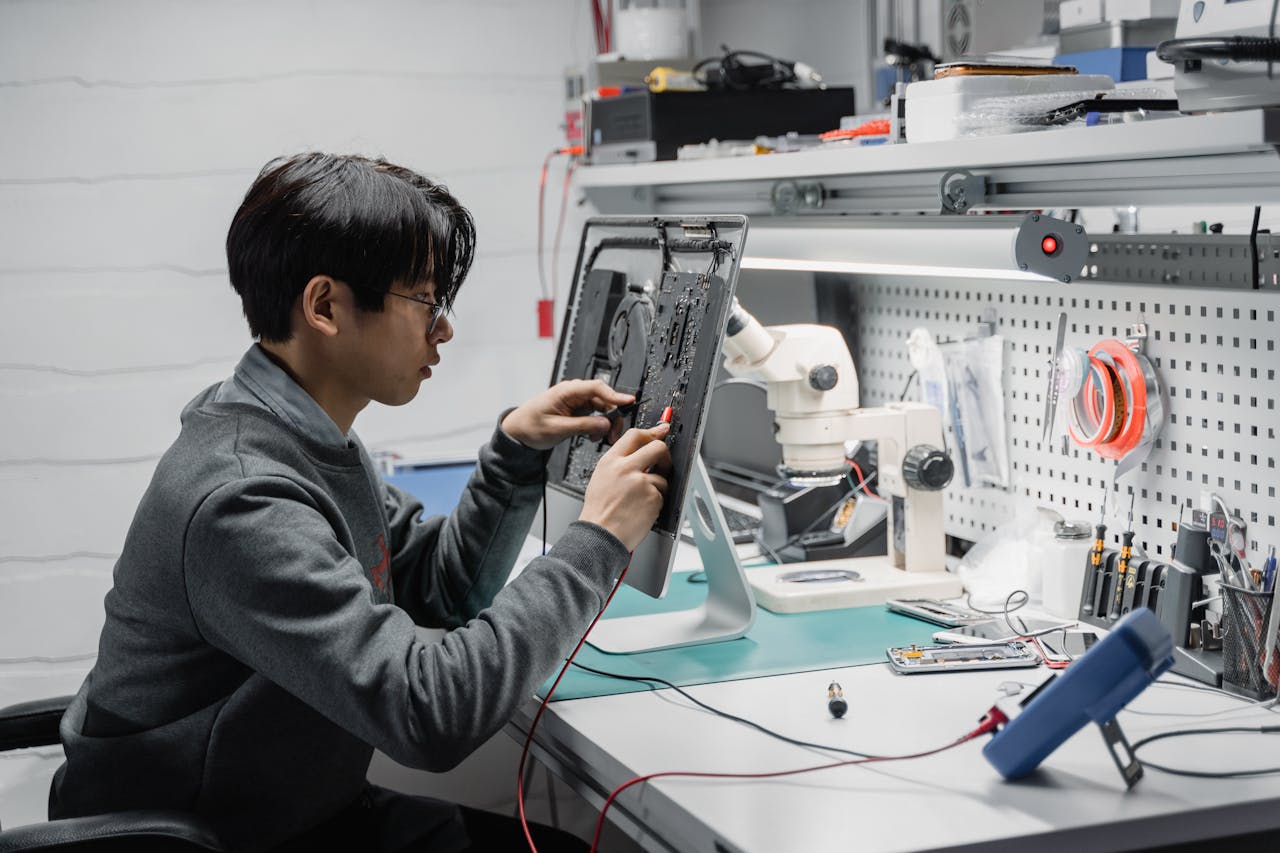 gallery-3 Focused young technician working on electronic repairs at a tech lab workspace.
